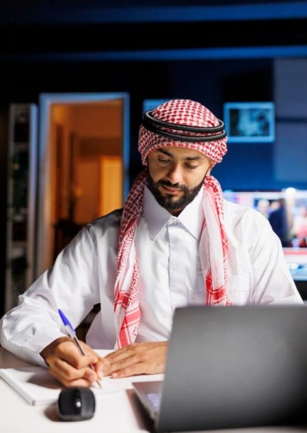 professional-muslim-guy-uses-technology-work-efficiently-office-browsing-online-writing-notes-from-laptop-youthful-arab-male-student-using-his-notebook-minicomputer-research-min